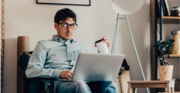 Man sitting and looking at his laptop while holding his coffee cup